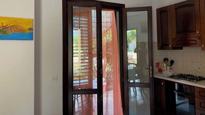 Una cocina con armarios de madera, una estufa a gas y un ventanal corredero que da a un espacio exterior.