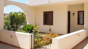Un balcón con un muro blanco, una puerta de madera y una ventana con contraventanas.