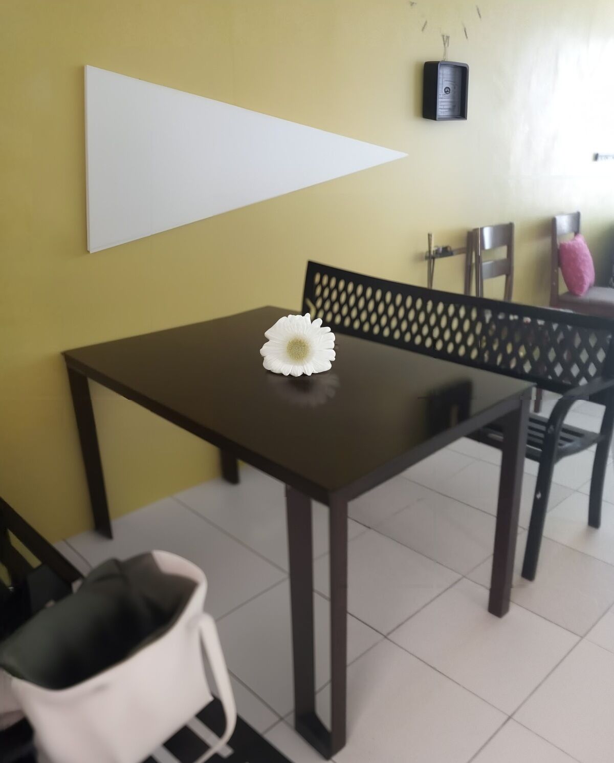 A dining area with a table and chairs, a white flower centerpiece, and a wall-mounted device.