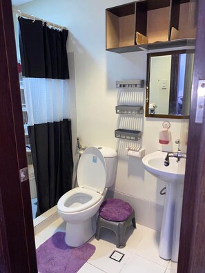 A small bathroom with a toilet, a sink, a mirror, and a shower curtain. - Chelsea Tower 2 (Muntinlupa)