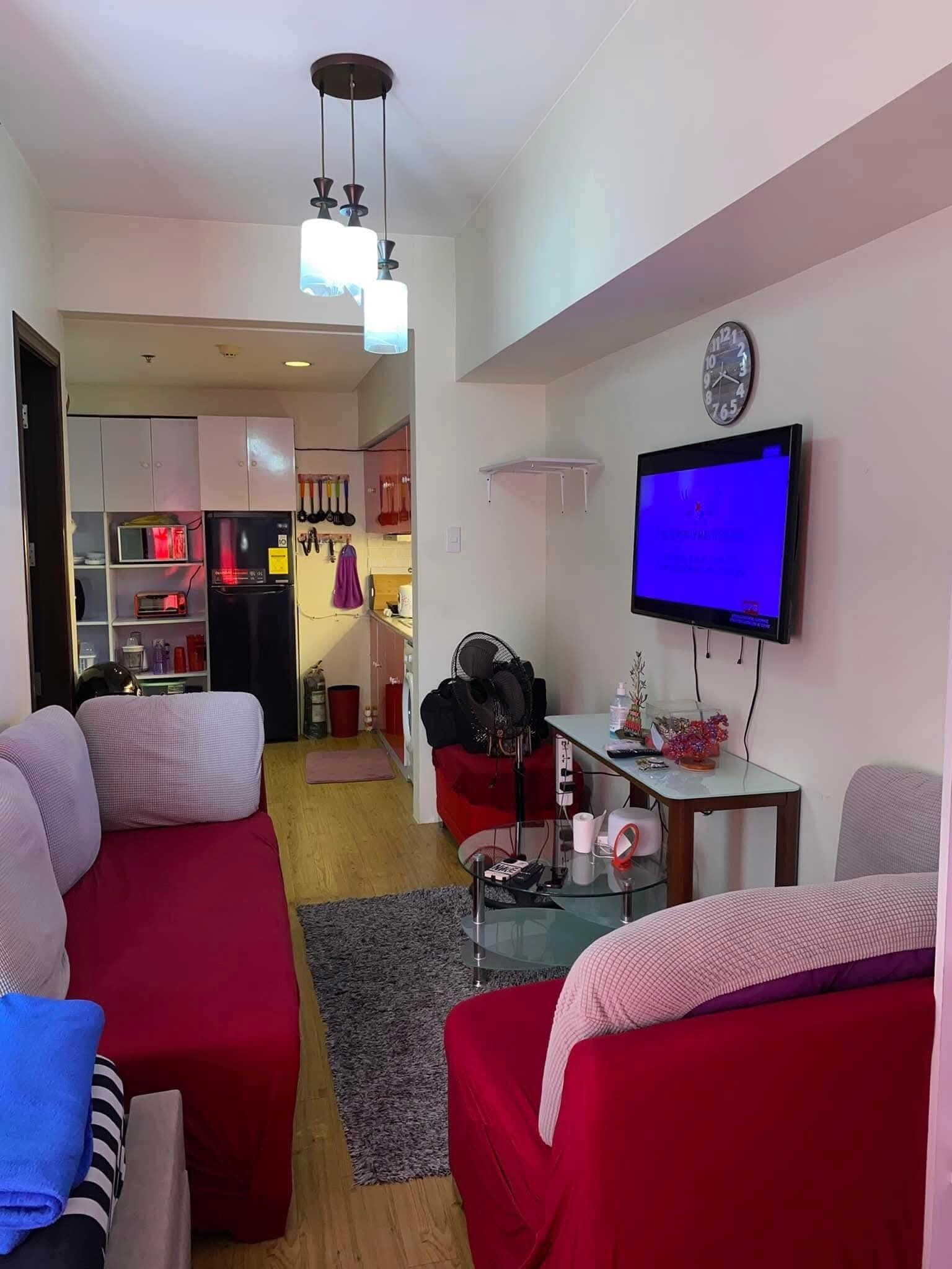 Un salon avec un téléviseur, des canapés rouges, une table basse en verre et, au fond, un coin cuisine.