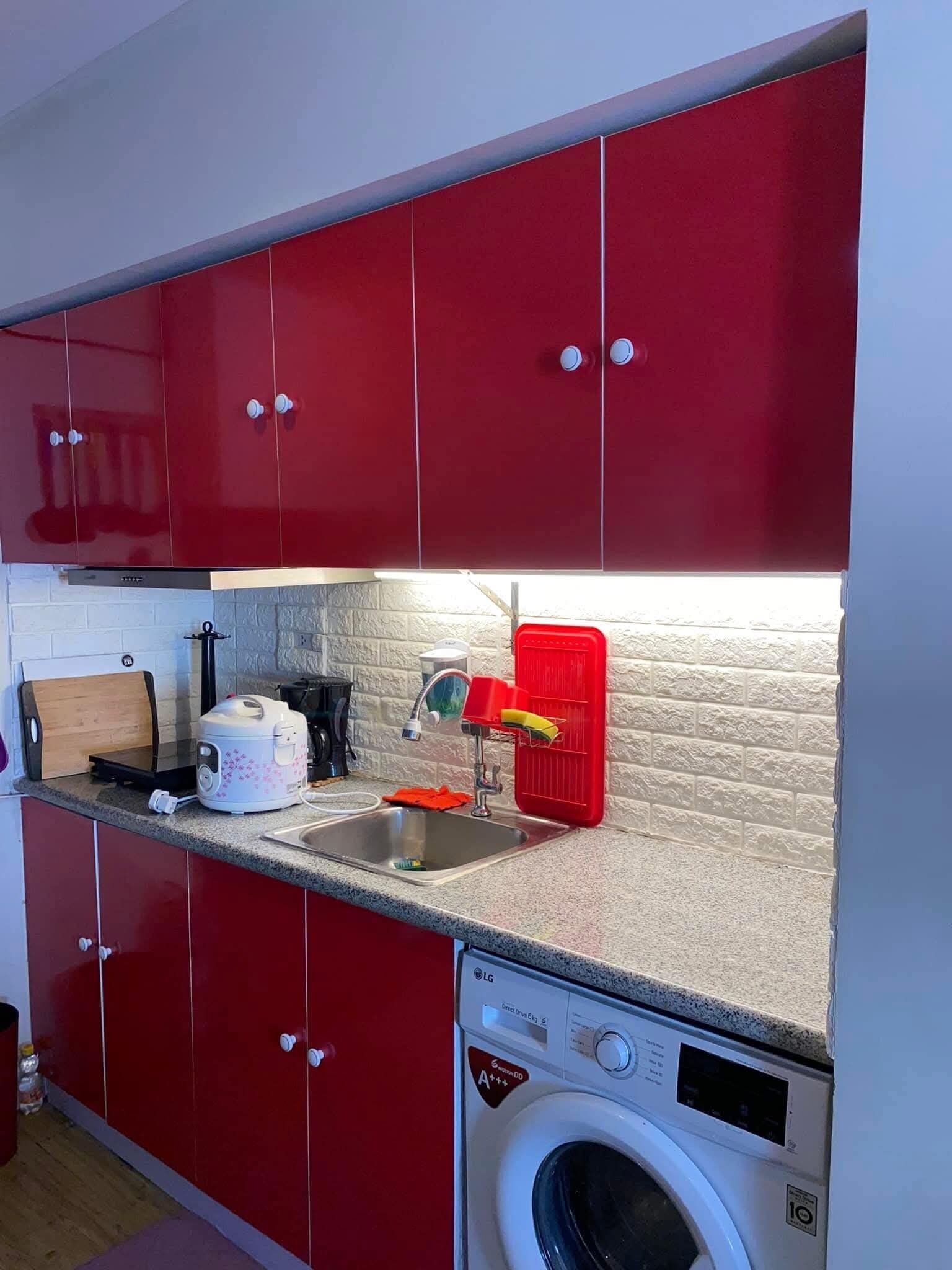 A compact kitchen with red cabinets, a built-in washing machine, a toaster, and a red drying rack.