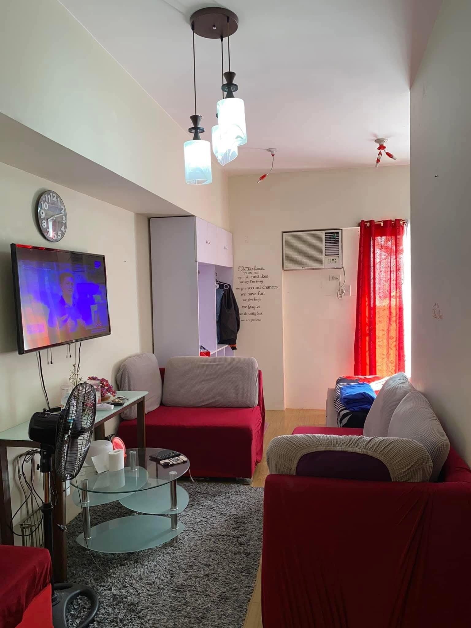 A living room with a TV, red sofas, a glass coffee table, and a ceiling fan.