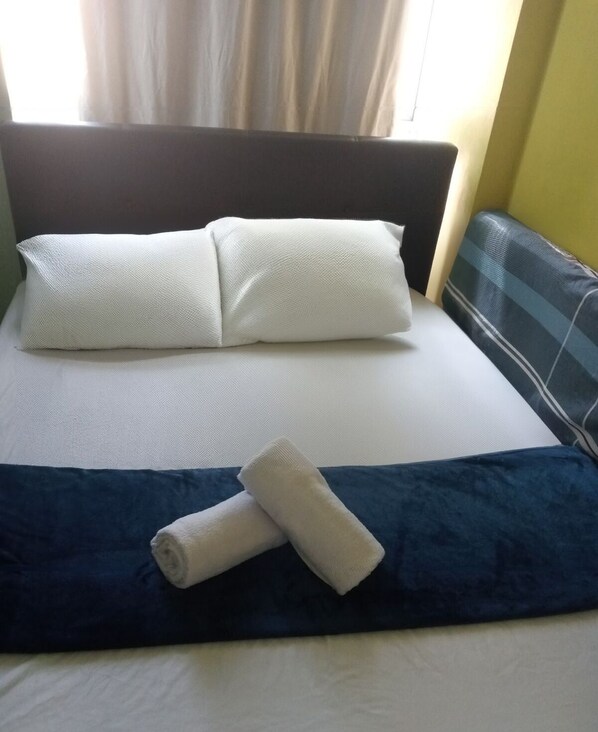 A bed with white pillows, a blue bedspread, and a rolled white towel. - Chelsea Tower 2 (Muntinlupa)