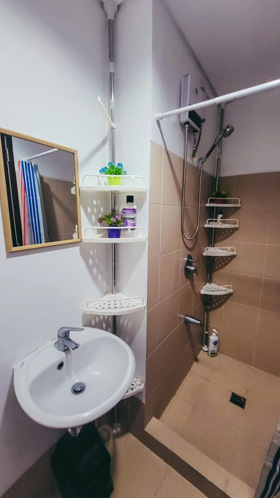 Un baño con lavamanos, espejo, ducha y repisas con artículos de aseo.