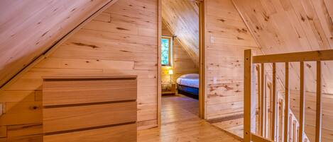 A wooden loft bedroom with a sloped ceiling, a bed, a nightstand, and a dresser.