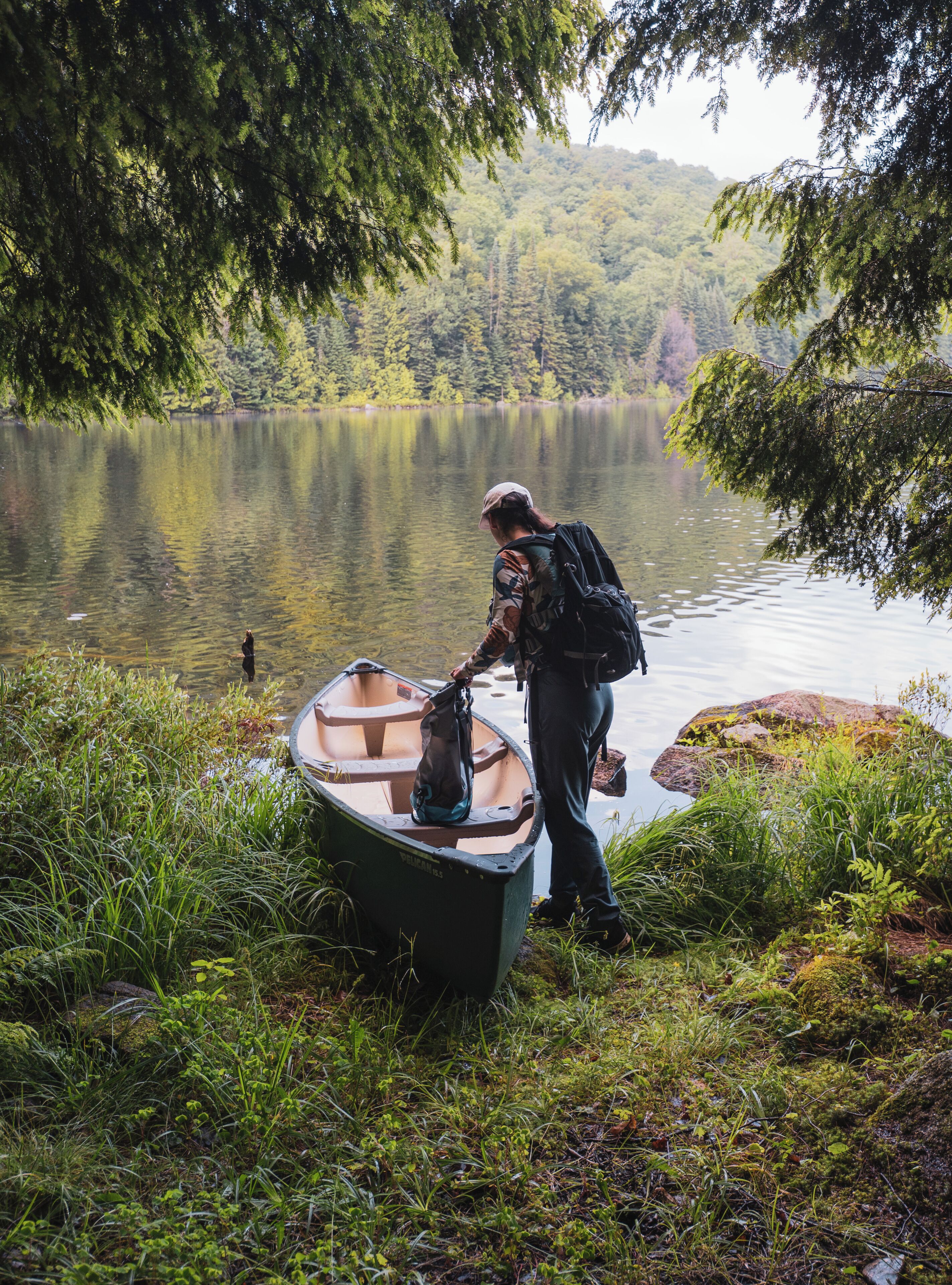 Una persona de pie junto a un bote pequeño en un lago rodeado de vegetación.