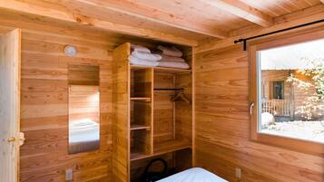 Una habitación de cabaña de madera con una cama, un armario empotrado y una ventana.