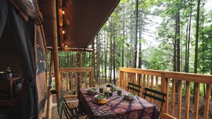 Une terrasse en bois avec une table dressée pour le repas, entourée d’une zone boisée.