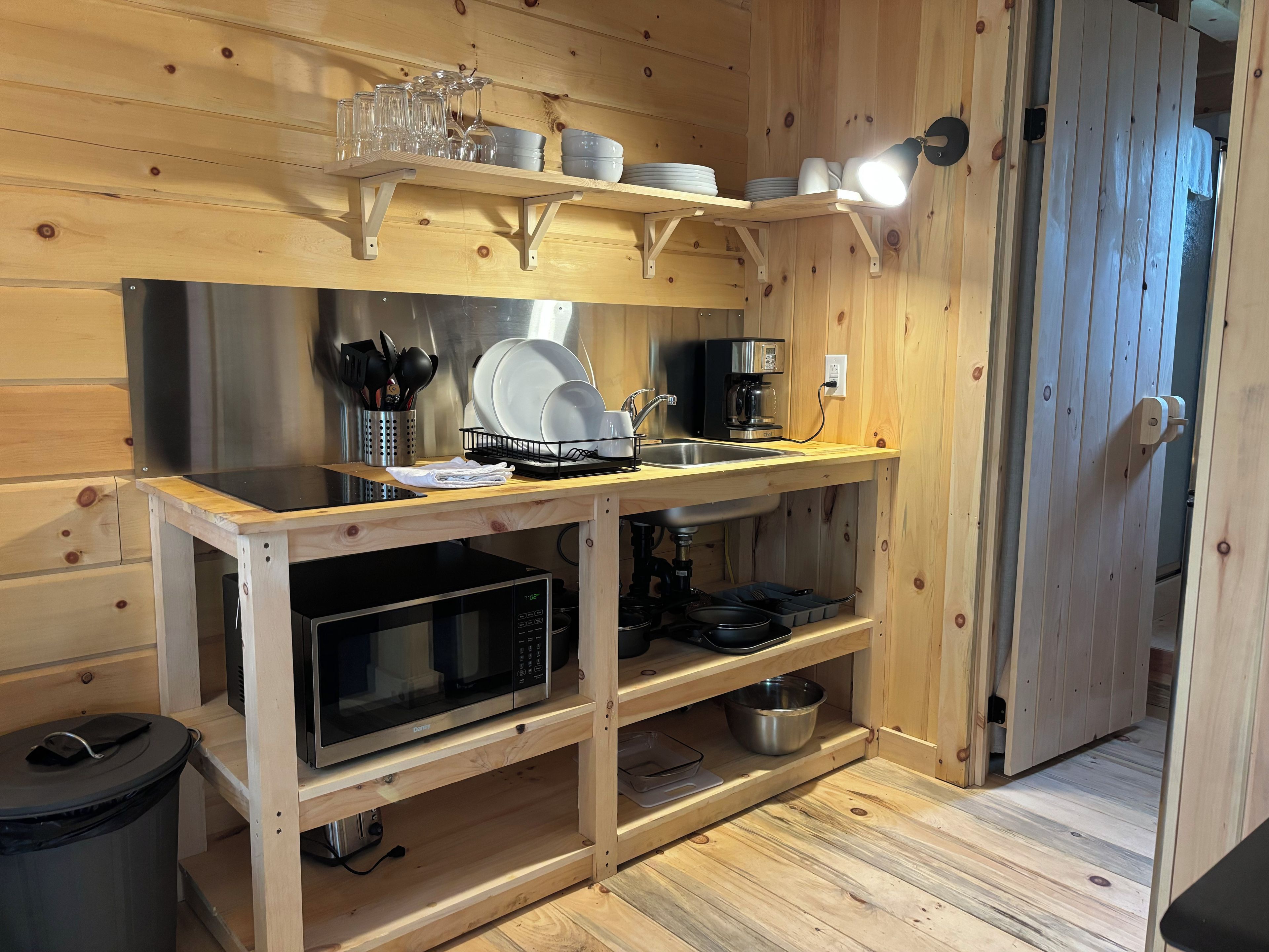 Ett kompakt kök med mikrovågsugn, kaffebryggare och hyllor i trä.