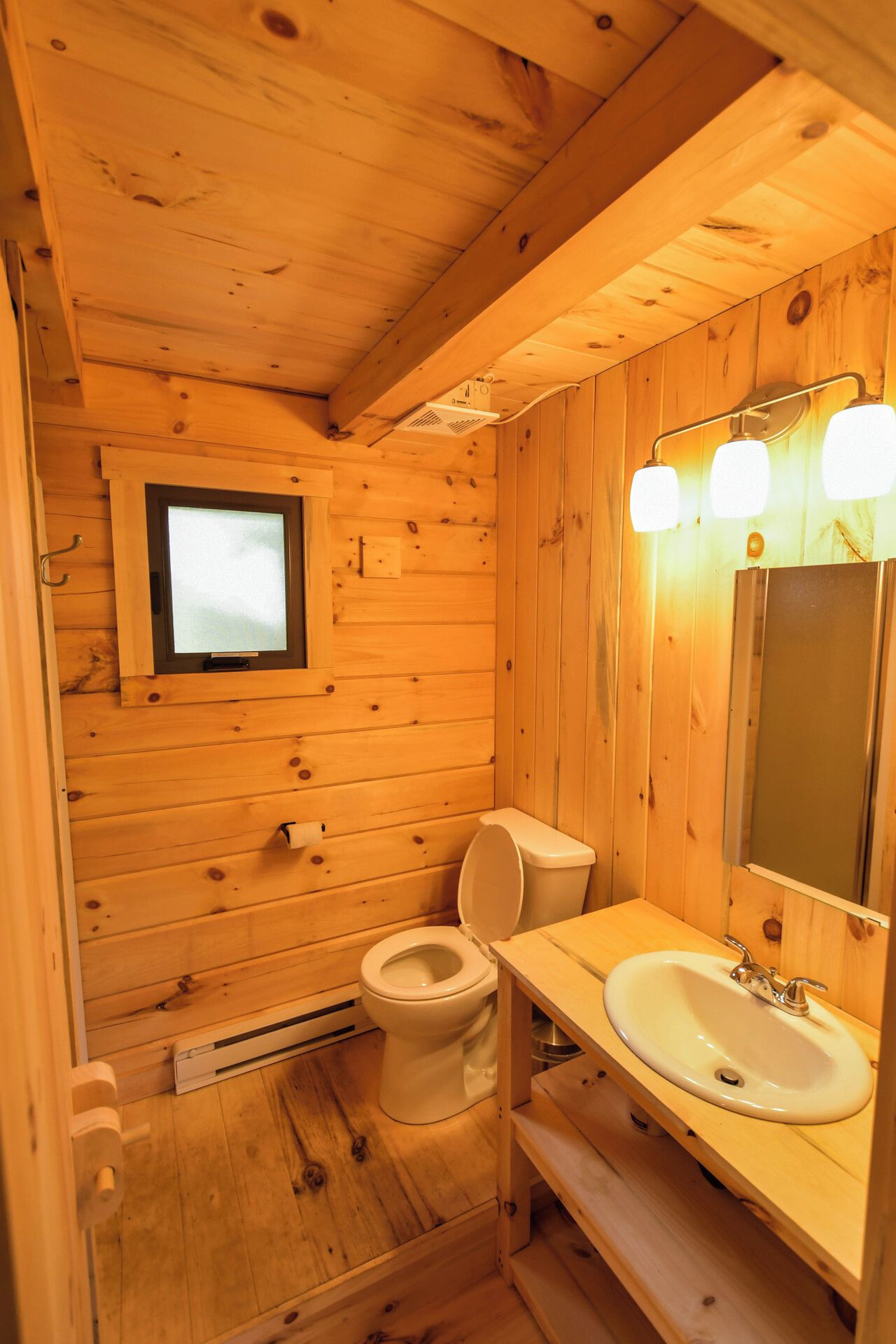 Une salle de bain rustique, aménagée dans une cabane en bois, avec des toilettes, un lavabo et une fenêtre.