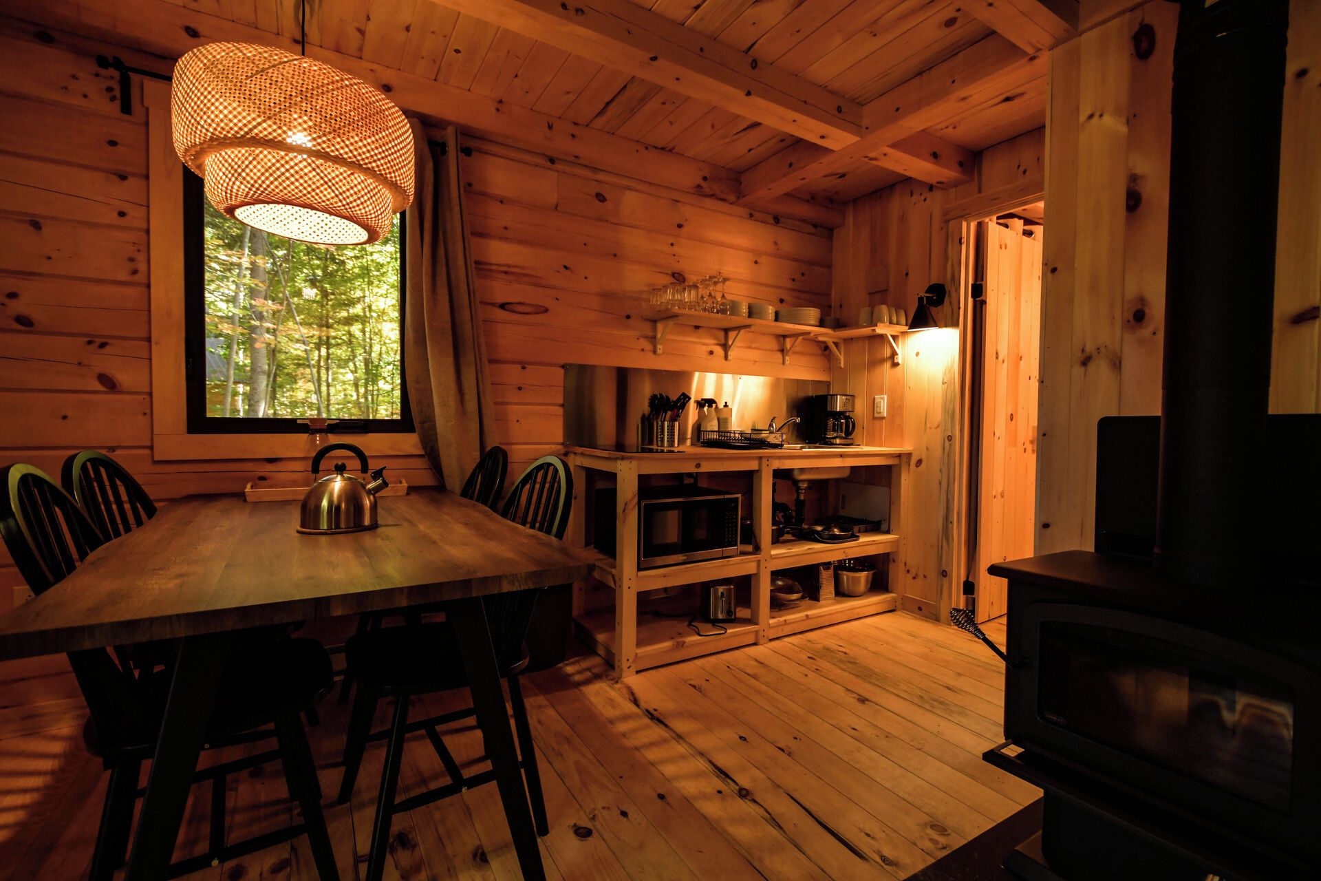 Un intérieur en bois comprenant une table à manger, des chaises, une bouilloire, un four à micro-ondes et une cuisinière.