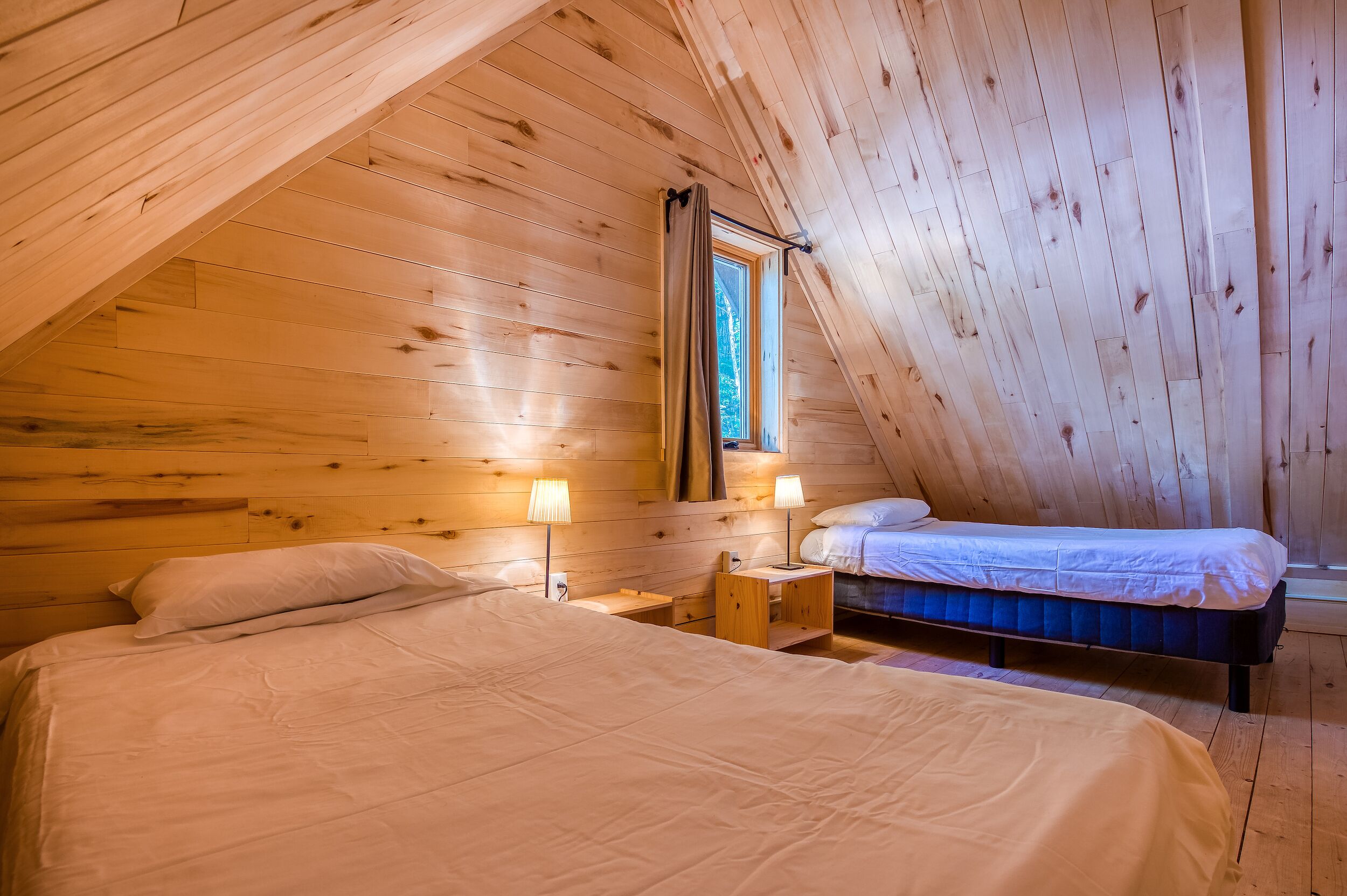 Ein gemütliches Schlafzimmer im Dachgeschoss mit Holzwänden, zwei Betten und einem Fenster.