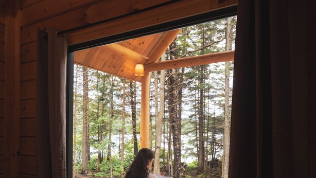 L’intérieur d’une cabane, avec une grande fenêtre donnant sur une forêt.
