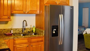 A kitchen with wooden cabinets, a stainless steel refrigerator, granite countertops, a ceiling fan, and a visible power outlet. - Easy Breezy Too! (Bonita Springs)