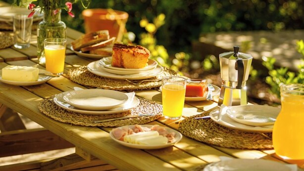 A wooden table set outdoors with plates, glasses, and a vase of flowers. - Casa Marmeleiro (Santiago do Cacém)
