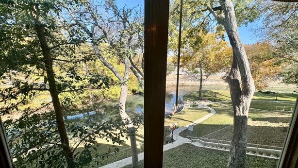 Vista a través de una ventana que muestra un parque con árboles, un estanque y un sendero para caminar.