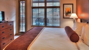 Une chambre d’hôtel avec un lit, une commode en bois, une télévision et une fenêtre avec des stores.