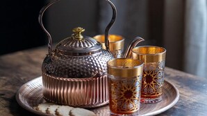 A tray with a metal teapot and three glasses on a wooden table.
