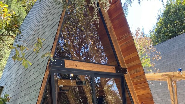 Una estructura de madera tipo cabaña en A con cerramiento de vidrio, un patio y un pequeño espacio de estar.