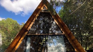 Una cabaña de madera triangular con un frente de vidrio y una terraza de madera.