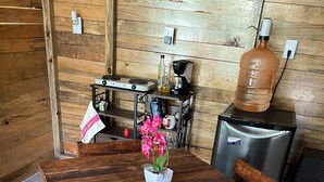 Una mesa de madera rústica con sillas, una orquídea en maceta y una cocina con electrodomésticos y dispensador de agua.