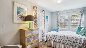 Un dormitorio con cama, mesita de noche, lámpara, cómoda y dos cuadros en la pared.