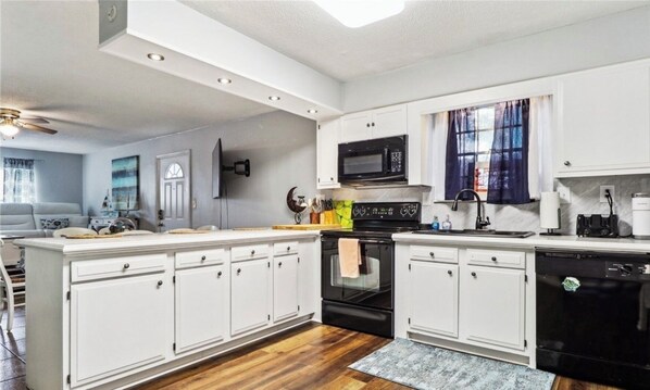 A modern kitchen with white cabinets, a black stove, a microwave, and a dishwasher. - Charming 2-bedroom house with AC, WiFi in awesome Tybee Island (Tybee Island)