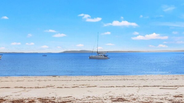 A beach with a clear sky, calm sea, and a distant landmass.