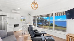 A modern living space with a kitchen, seating area, and large windows offering a view of the sea.