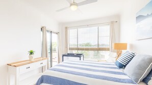A bedroom with a bed, a desk, a chair, a window with blinds, and a ceiling fan.