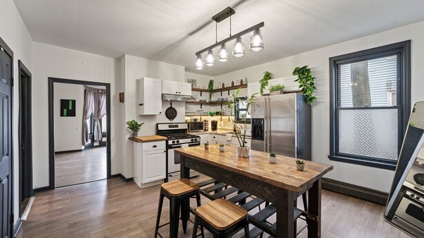 A modern kitchen with a central island, bar stools, a stainless steel refrigerator, and a hanging light fixture.