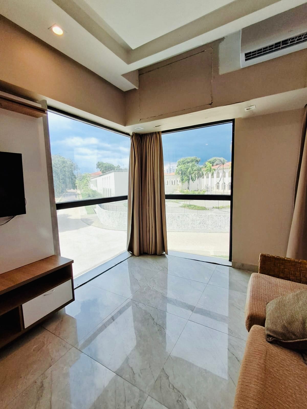 A spacious living room with a large window, a flat-screen TV, and a comfortable sofa.