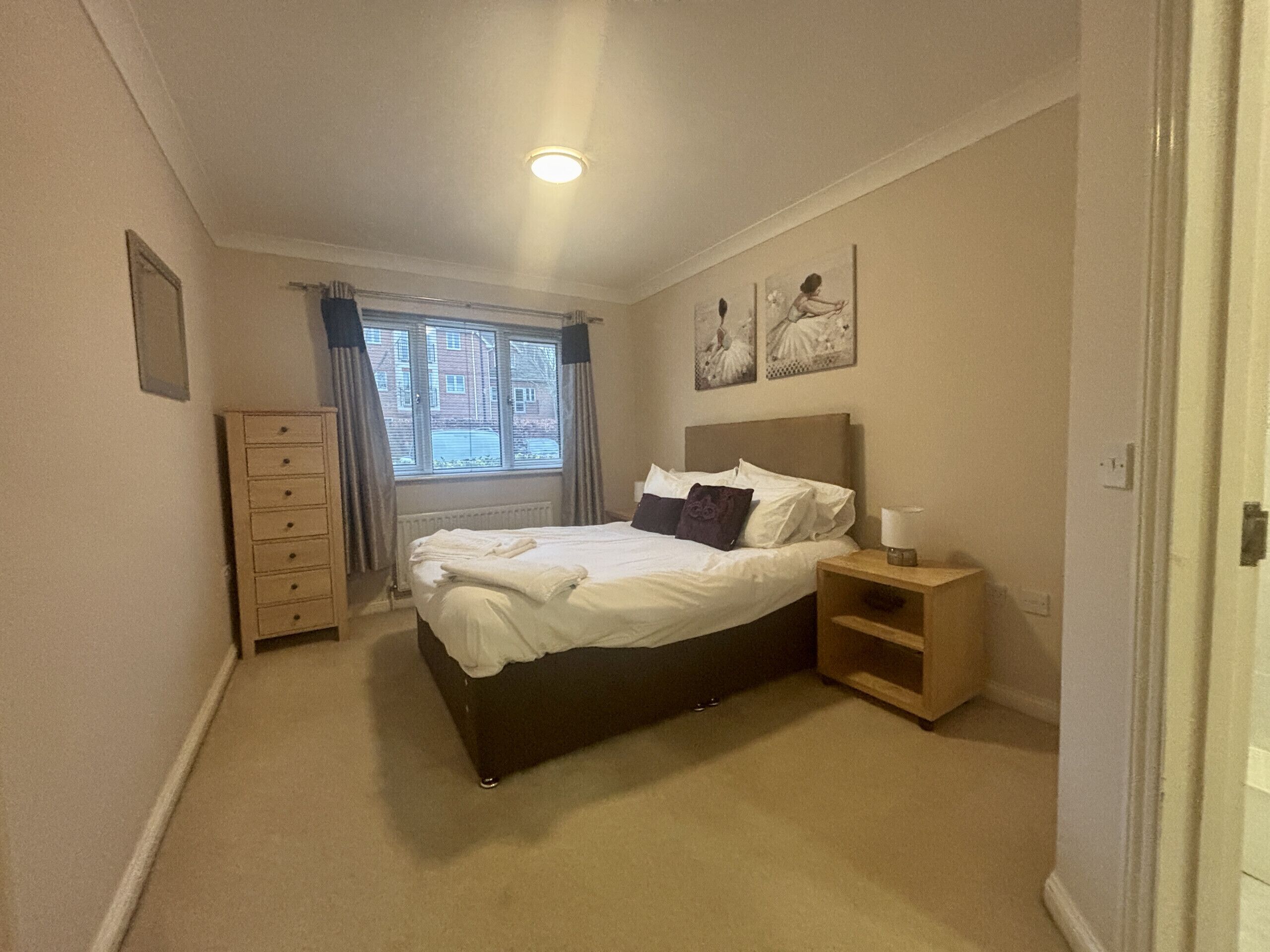 Un dormitorio con cama, cómoda, mesita de noche y ventana con cortinas.