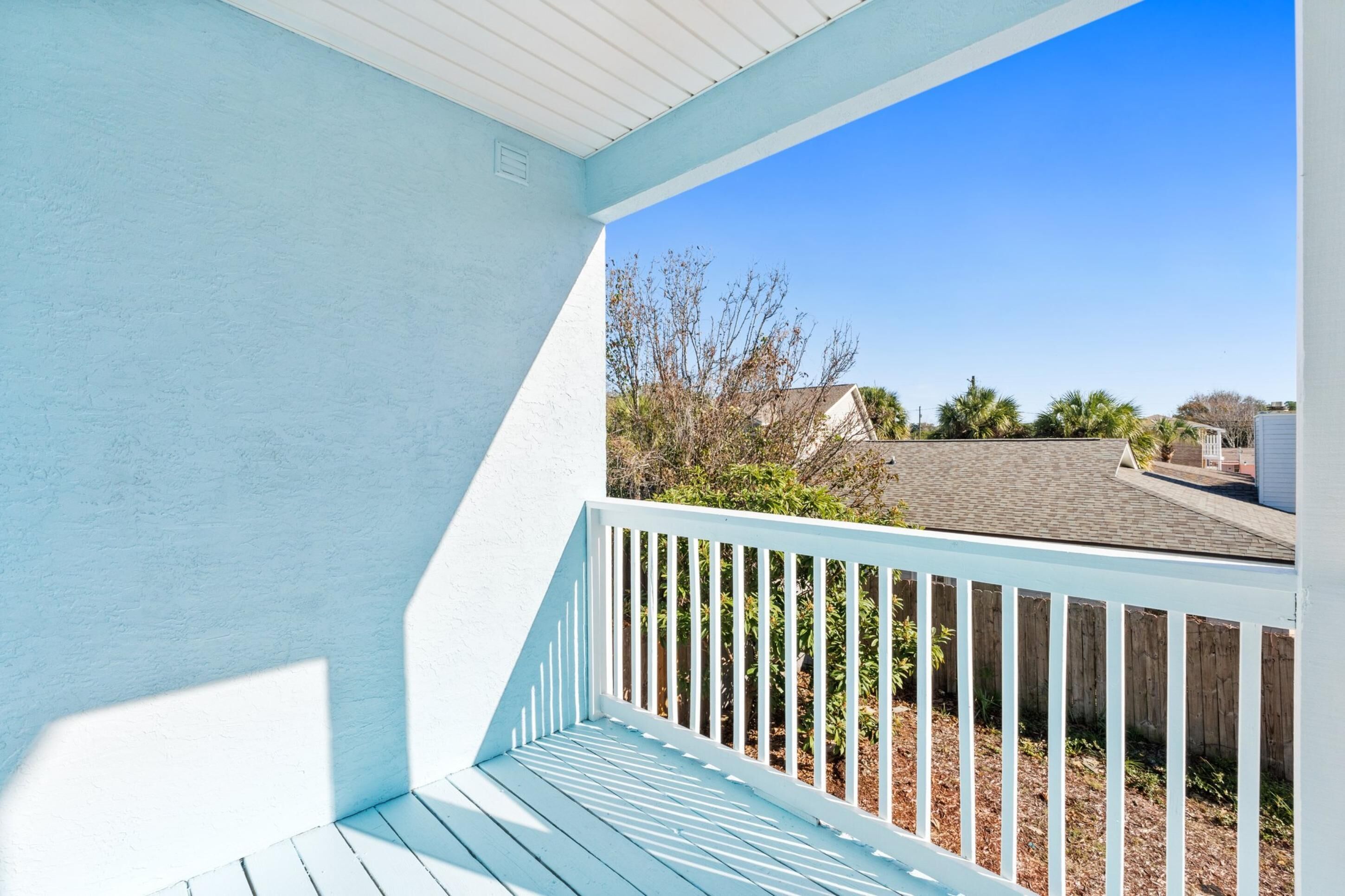 Une véranda couverte avec une balustrade blanche, un ciel d’un bleu limpide et une vue sur un quartier résidentiel avec des maisons et des arbres.