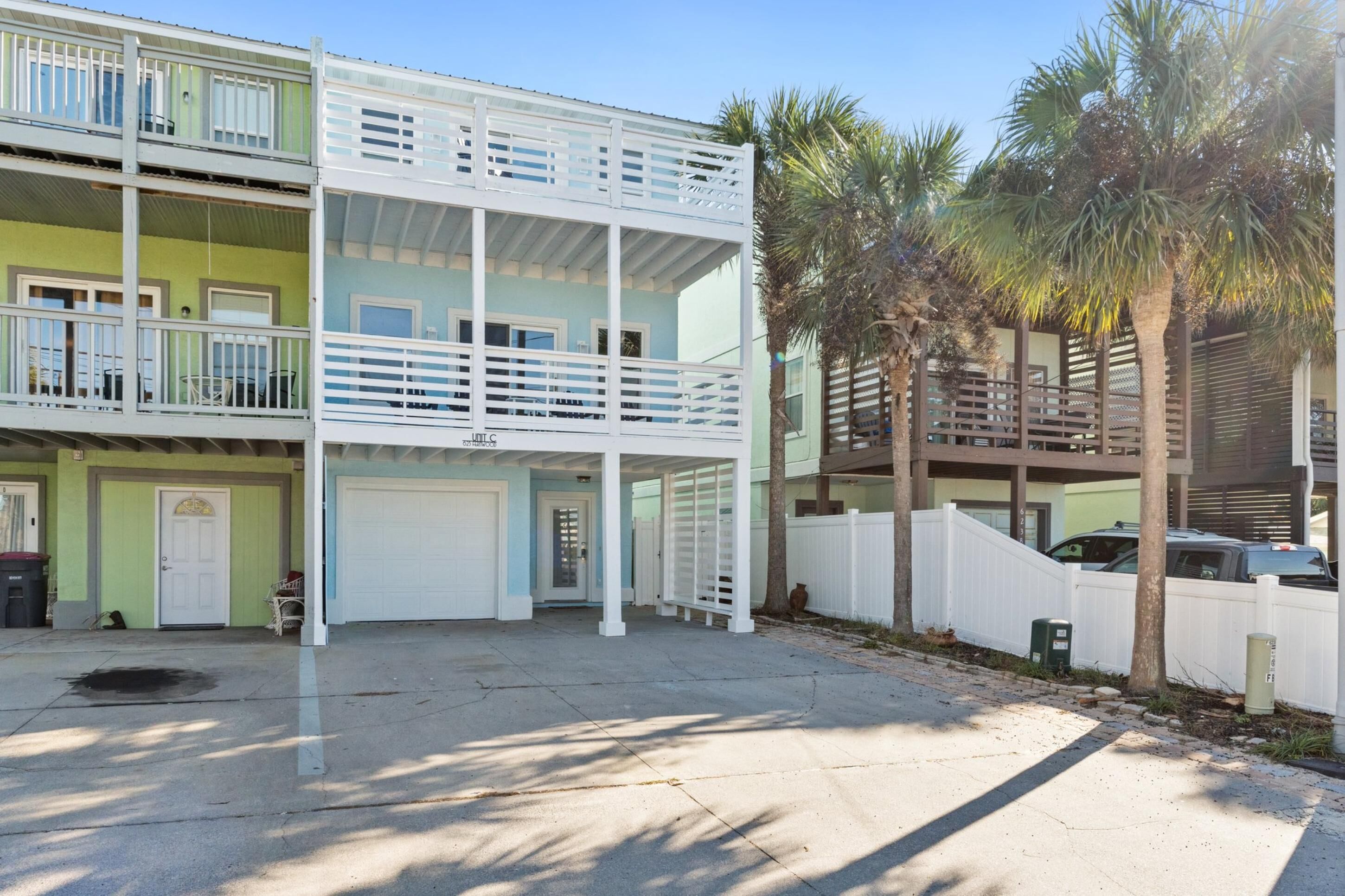 A multi-story building with a garage, a balcony, and a fenced area with palm trees.
