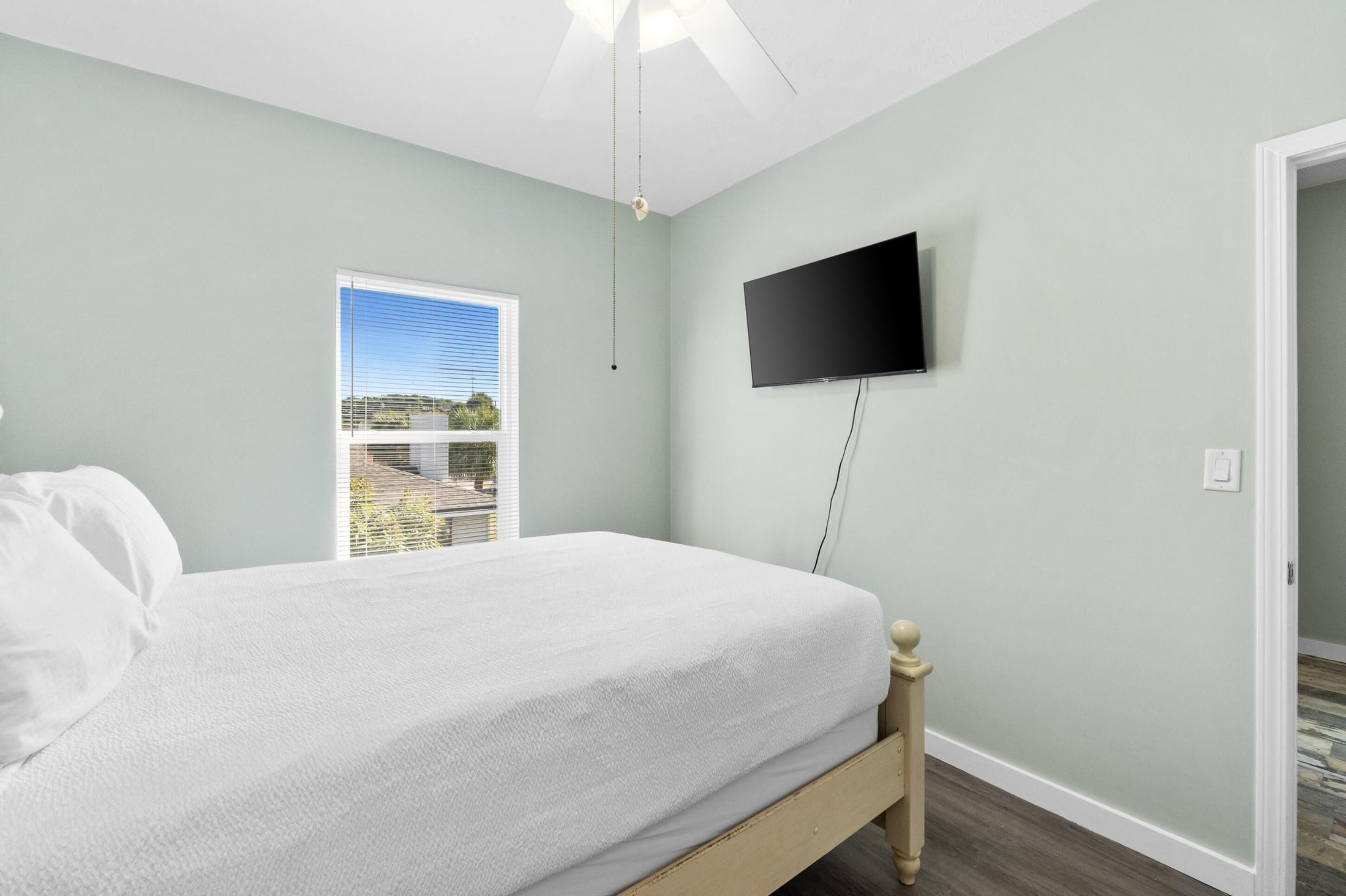 A bedroom with a bed, a television mounted on the wall, and a window with blinds.