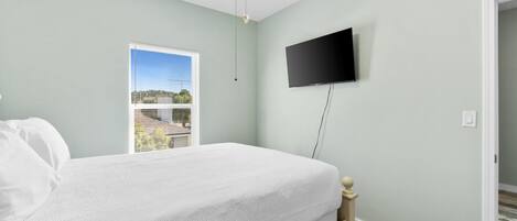 A bedroom with a bed, a television mounted on the wall, and a window with blinds.