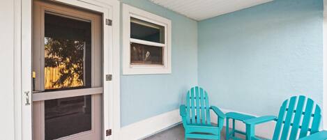 Een veranda met turquoise Adirondack-stoelen, een tafeltje en een deur met een raam.