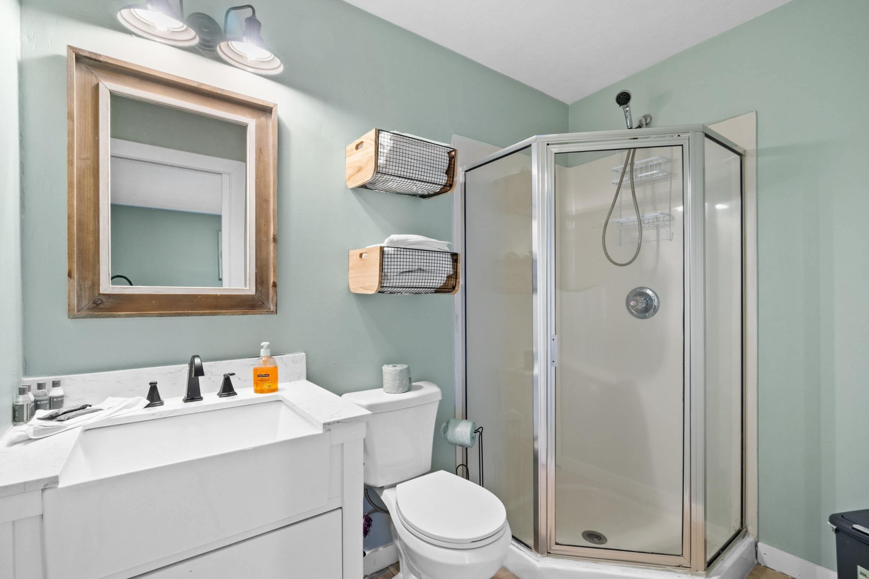 A bathroom with a white sink, mirror, toilet, and a glass-enclosed shower.