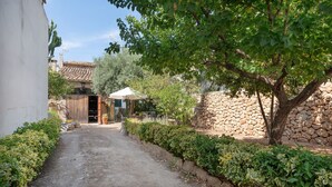 A narrow, paved pathway flanked by neatly trimmed hedges and a stone wall, leading to a rustic building with a tiled roof.