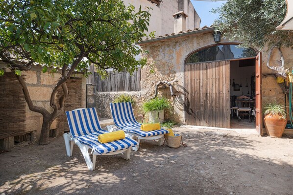 A rustic outdoor seating area with two striped lounge chairs, a potted plant, and a wooden door leading to a room.
