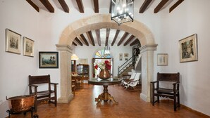 A spacious room with a high ceiling, exposed wooden beams, and a central archway. There are multiple chairs and a table with a copper pot.