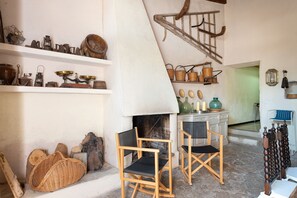 A rustic interior with wooden shelves displaying vintage kitchenware, a fireplace, and a dining area with wooden chairs.