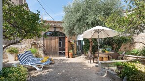 A rustic outdoor seating area with a table and chairs, a striped lounge chair, and a large umbrella providing shade.