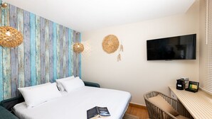 Un dormitorio con cama, televisor, escritorio y una silla de mimbre.