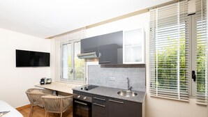Cocina compacta con horno empotrado, un lavamanos y un televisor de pantalla plana montado en la pared.