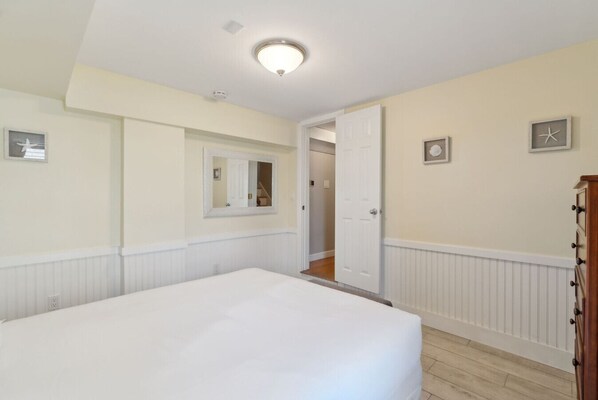 Une chambre avec un grand lit, une porte donnant sur un couloir et un miroir au mur.