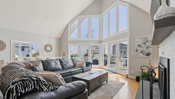 A spacious living room with a high ceiling, large windows, a fireplace, and a view of the outside.