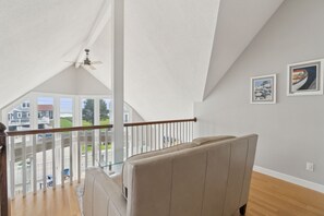 Un balcon spacieux offrant une vue sur un quartier résidentiel, un ventilateur de plafond et deux tableaux encadrés accrochés au mur.